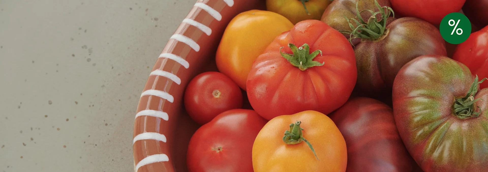 Verschiedene reife rote, gelbe und alte Tomaten in einer Terrakottaschale mit grünem Prozentzeichen.