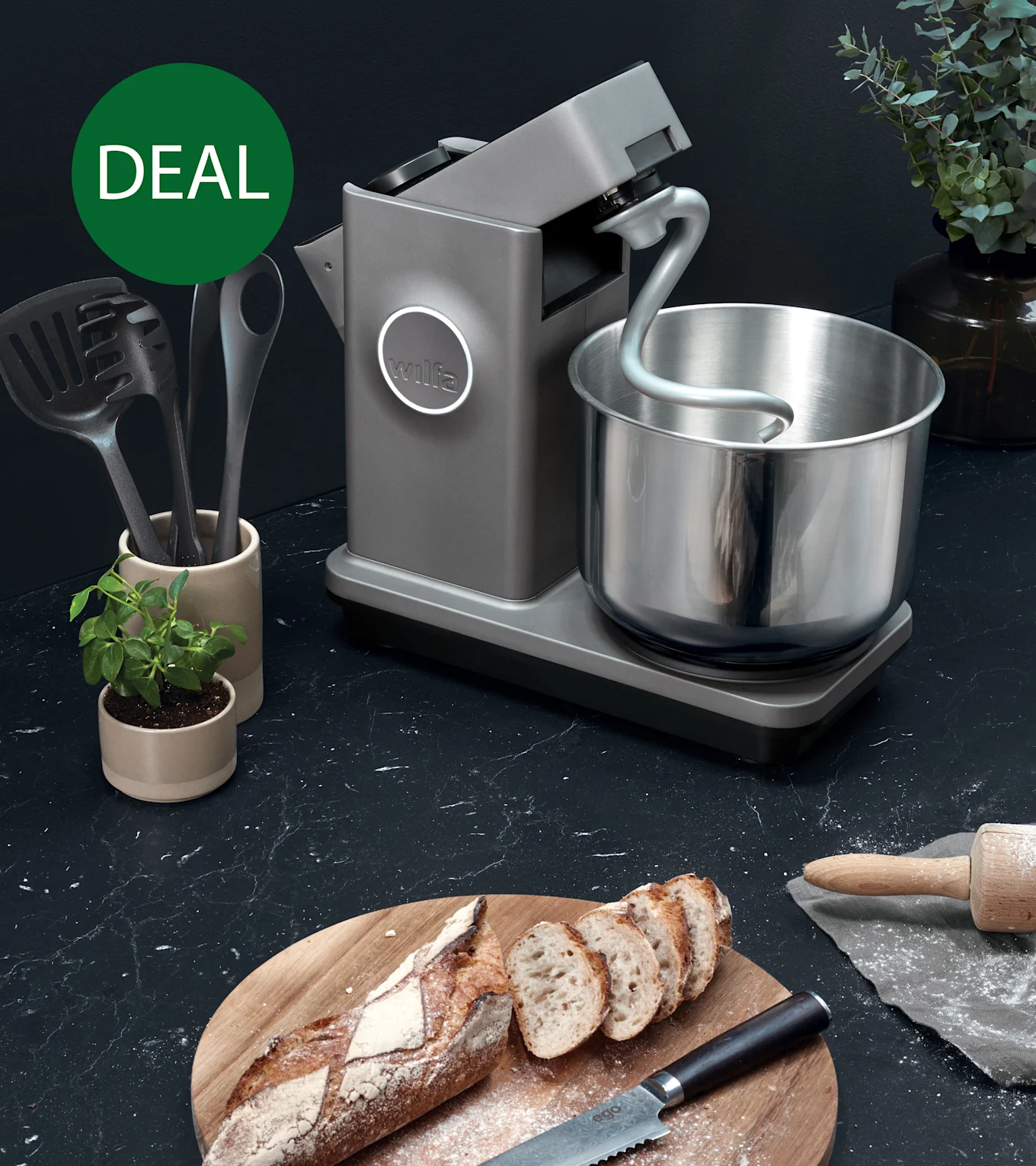Graue Küchenmaschine mit Knethaken und Edelstahlschüssel auf dunkler Arbeitsplatte mit geschnittenem Brot, markiert mit grünem 'DEAL'-Kreis.
