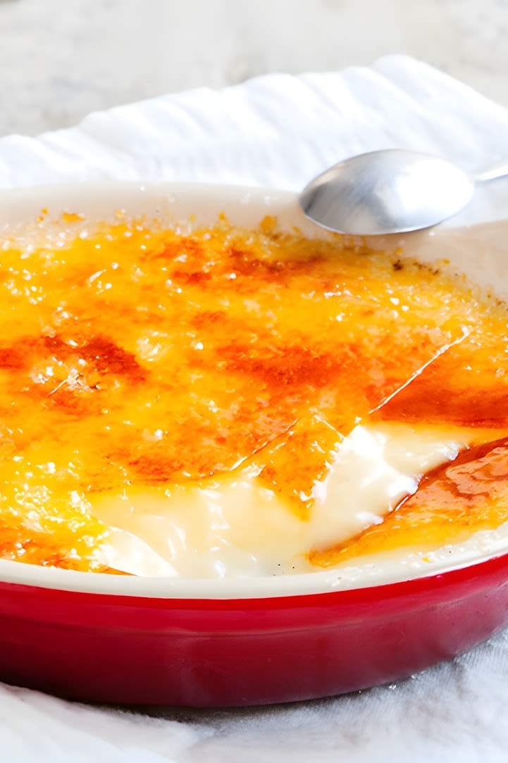 Hier sehen Sie eine Nahaufnahme einer perfekten Crème Brûlée mit goldener Kruste in einem orangefarbenen Schälchen von Le Creuset.