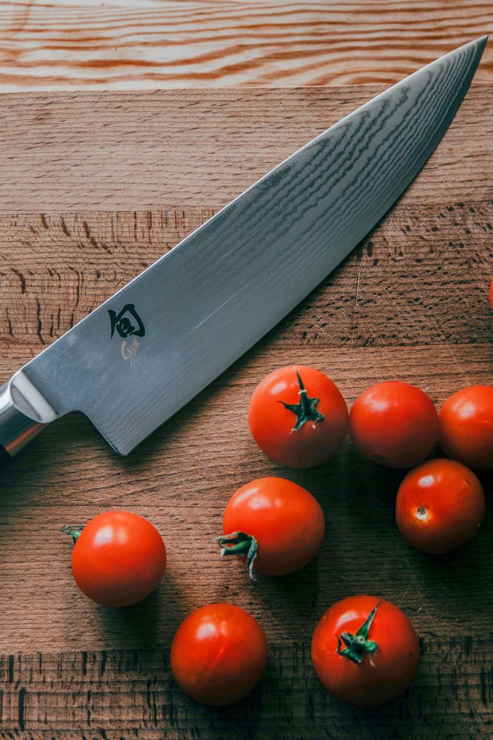 Eine Nahaufnahme eines Kai Shun Gyuto Messers auf einem hölzernen Schneidebrett mit Tomaten.